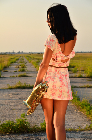 A girl with her back in a dress holding near a hip saxophoneの写真素材