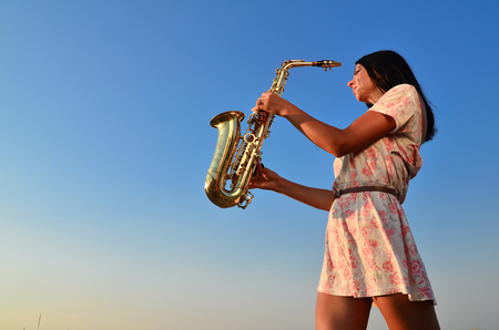 Young girl holding a saxophone on blue sky backgroundの写真素材
