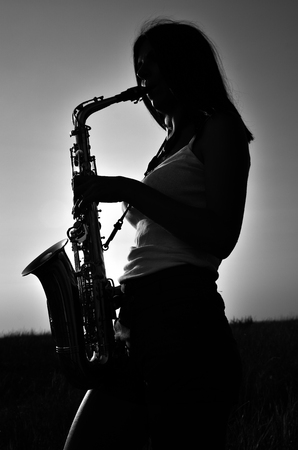 A young girl plays the saxophone on the nature of black and white photosの写真素材