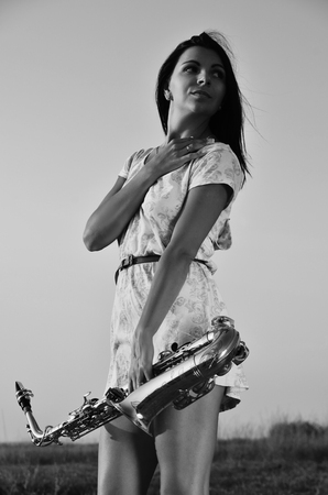 Young girl holding a saxophone and watching the sunset. Black-and-white photographの写真素材