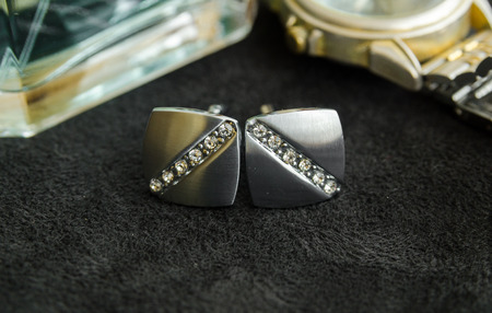 Silver cufflinks with precious stones on black matter between perfumes and gilded watchの写真素材