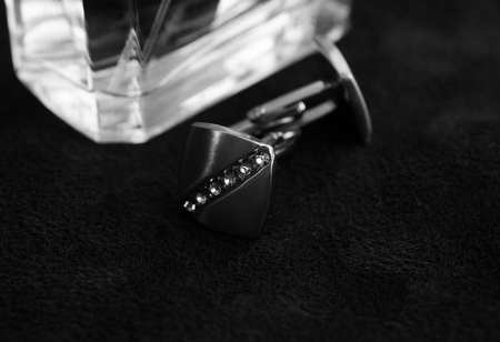 Silver cufflinks with rhinestones on a black background next to the perfume bottle, the horizontal black-and-white photoの写真素材