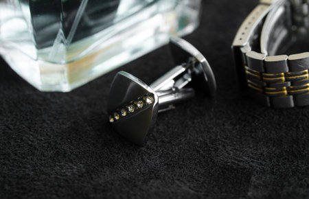 Silver cufflinks with crystals on black background next to a bottle of perfume and watchesの写真素材