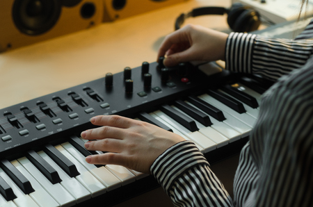 A woman in a striped shirt plays the synthesizer and sets it up. Next to her headphones, a music console and speakers. Side viewの写真素材