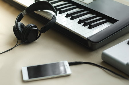 Headphones, synthesizer and a telephone lying on a beige background next to the music console. Side viewの写真素材