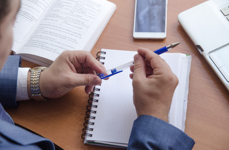 A businessman holds a pen in his hands and is going to write in a notebook. Next is a notebook, phone and book.の写真素材