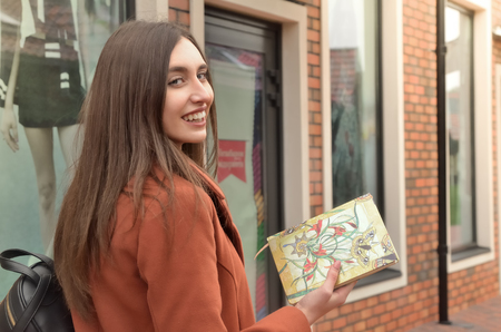 An attractive girl stands at the windows, holding a beautiful notebook in her hands. A backpack on the shoulder, split hair. Horizontal photoの写真素材