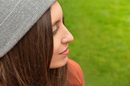 Portrait of a beautiful young European woman against green background. Dressed in a hat, turned into a profile. Easily smilesの写真素材