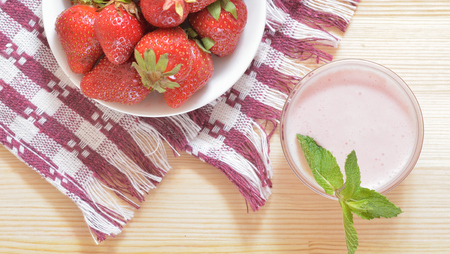 Red large strawberries on a white plate, pink sauce in a saucepan. On a wooden table on a tablecloth. Top viewの写真素材