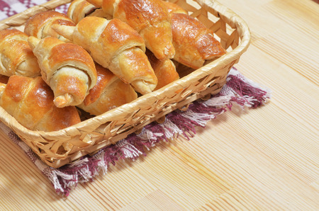 Wicker basket with home-made fresh croissants is on a napkin on a light wooden table.の写真素材