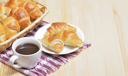 Fresh croissants on a plate and in a basket on a wooden table, a cup of coffeeの写真素材