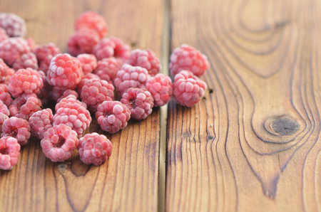 Raspberries covered with frost lie on a wooden background on the left side