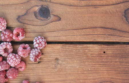 Several frozen raspberries, covered with fruit, lie on the wooden background from the top left