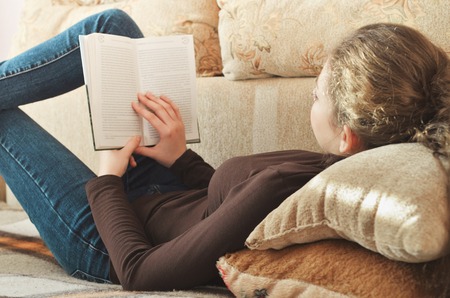 Young beautiful girl reading a book on the couchの写真素材
