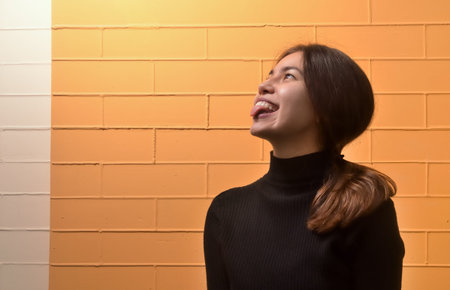The happy young girl of Asian appearance happily shows tongue on a yellow brick background