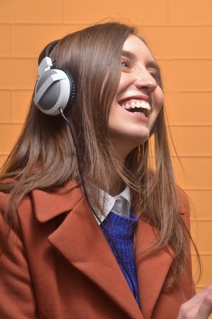 Young happy woman with headphones listening music over orange backgroundの写真素材