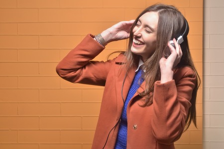 Pretty blonde girl laughing while listening music on big white headphones isolated on ogange - copy spaceの写真素材