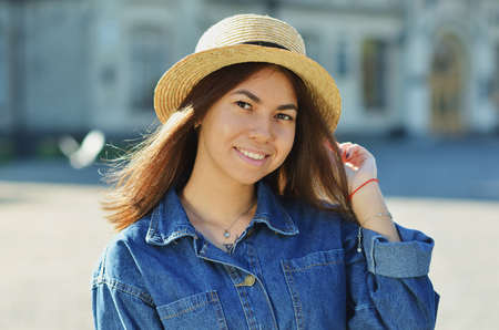 Portrait of a happy cheerful girl in a summer hat, holding in one hand his hat, in the background of the University campusの写真素材