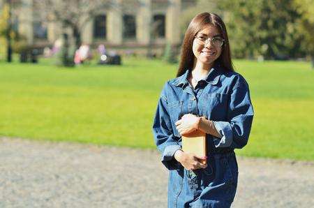 Happy successful pretty woman crossing hands and smiling near campus with her bookの写真素材