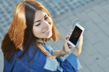 The girl sits on a bench and listens to music with headphones smiling with her eyes closedの写真素材