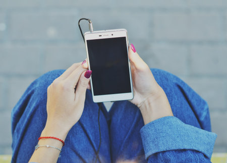 Smartphone close-up in the hands of a girl dressed in denim clothing that listens to music in...