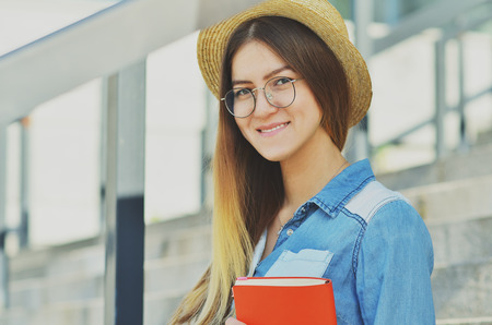 Portrait of a young girl who is wearing a straw hat holding an orange notebook in her hands and smilingの写真素材