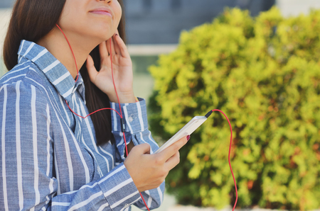 Young girl student holding a phone and listening to music on the street in the Parkの写真素材