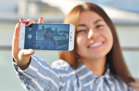 A girl student of Asian appearance smiles beautifully and makes a selfie while on the streetの写真素材