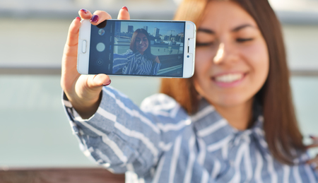 Attractive girl student smiles with her eyes closed and takes a selfie at arm's lengthの写真素材