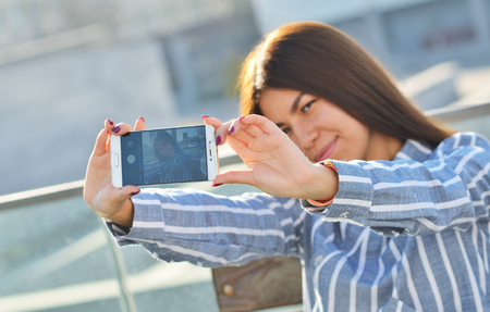 A young girl photographs herself with a phone, walking around the cityの写真素材