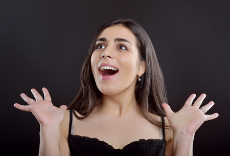Beauty portrait of a young girl who surprisingly shrugs to the side and stands on a black backgroundの写真素材