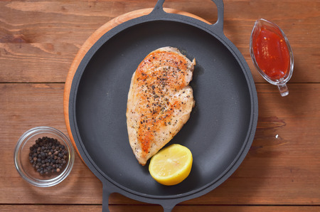 Fried chicken breast with lemon in a pan, spices and a sauce on a wooden tableの写真素材