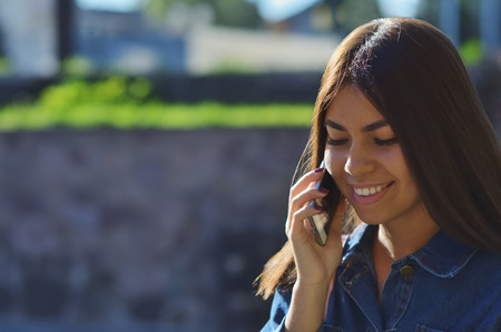 Portrait of a young attractive girl who talks on the phone on the street and smilesの写真素材