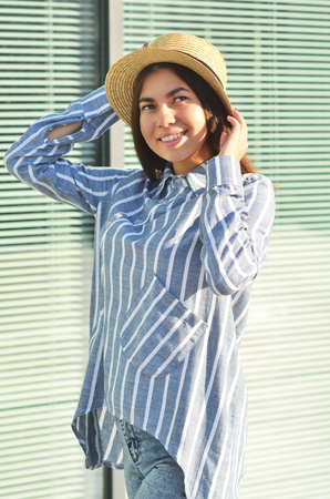 Portrait of a young girl is standing near the wall in a hat, and she is dressed in blue striped shirtの写真素材