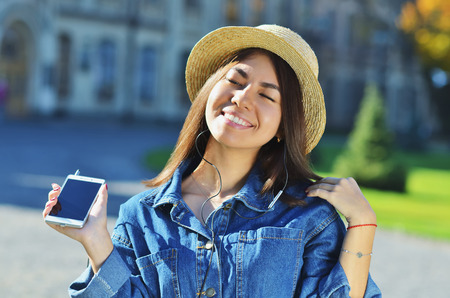 A young girl of Asian appearance enjoys life and listens to music raising her head up and smiling with her eyes closedの写真素材
