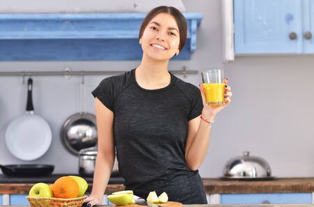 A young asian fitness girl makes a glass of orange juice at the home. She is happy and smilingの写真素材