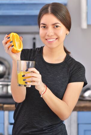 A sports asian woman in a black t-shirt makes a orange juice in the kitchen. Horisontal photoの写真素材