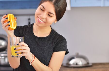 Sport Asian woman in a black t-shirt squeezes orange juice in the kitchen. Horizontal photoの写真素材