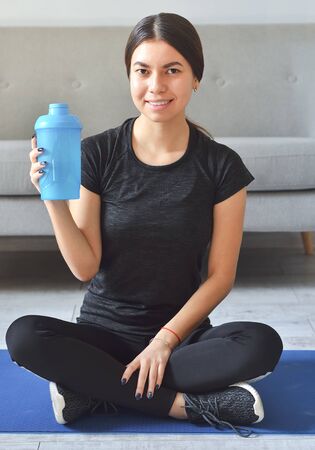 Sport at home concept. Smiling young asian girl is sitting on mat with sports equipment at homeの写真素材