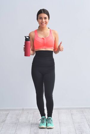 Young happy fitness girl with sporty body drink water at studio on a white background. Beautiful fit Girl. Fitness model in pink sportswear.の写真素材