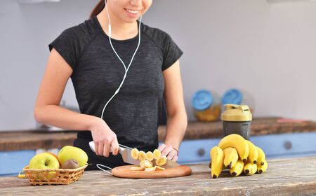 Young woman listening to music and making healthy smoothie at home in the kitchenの写真素材