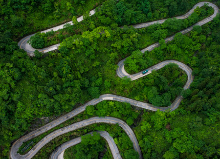 An awe-inspiring aerial view of a winding road snaking through lush green mountains.の写真素材