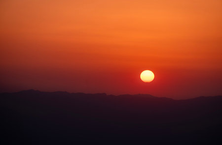 The sun descends, casting a dramatic silhouette against the dark mountain range. A moment of pure beauty.の写真素材