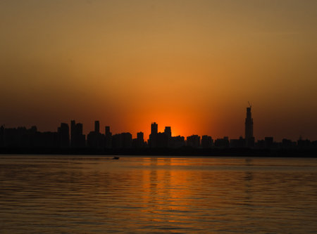 A calm lake reflecting the last golden rays of sunset, set against the silhouette of distant cityscapeの写真素材