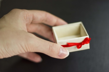 A woman hand holding a white gift box with red ribbon. Black backgroundの写真素材