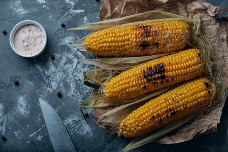 grilled corn on the right with sauce and a knife sprinkled with pepperの写真素材