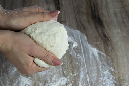 Woman kneading dough with her hands on wooden table on dark background.の写真素材