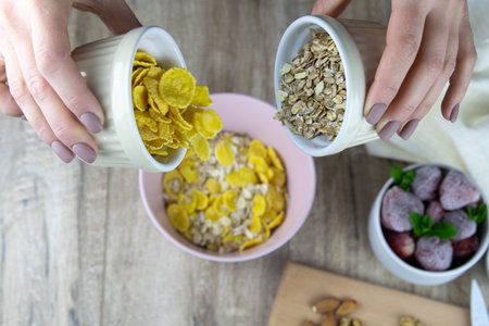 Healthy breakfast. Grey ceramic bowl with granola, strawberry and nuts in woman's hands. Diet and...