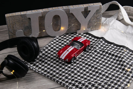 Toy red car on the on a black white checkered bag next to headphones and in the background a plaque...