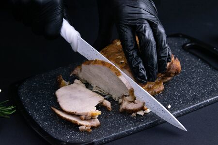 Slicing juicy beef steak by knife in chef hands closeup. Food cooking concept. Dark black backgroundの写真素材